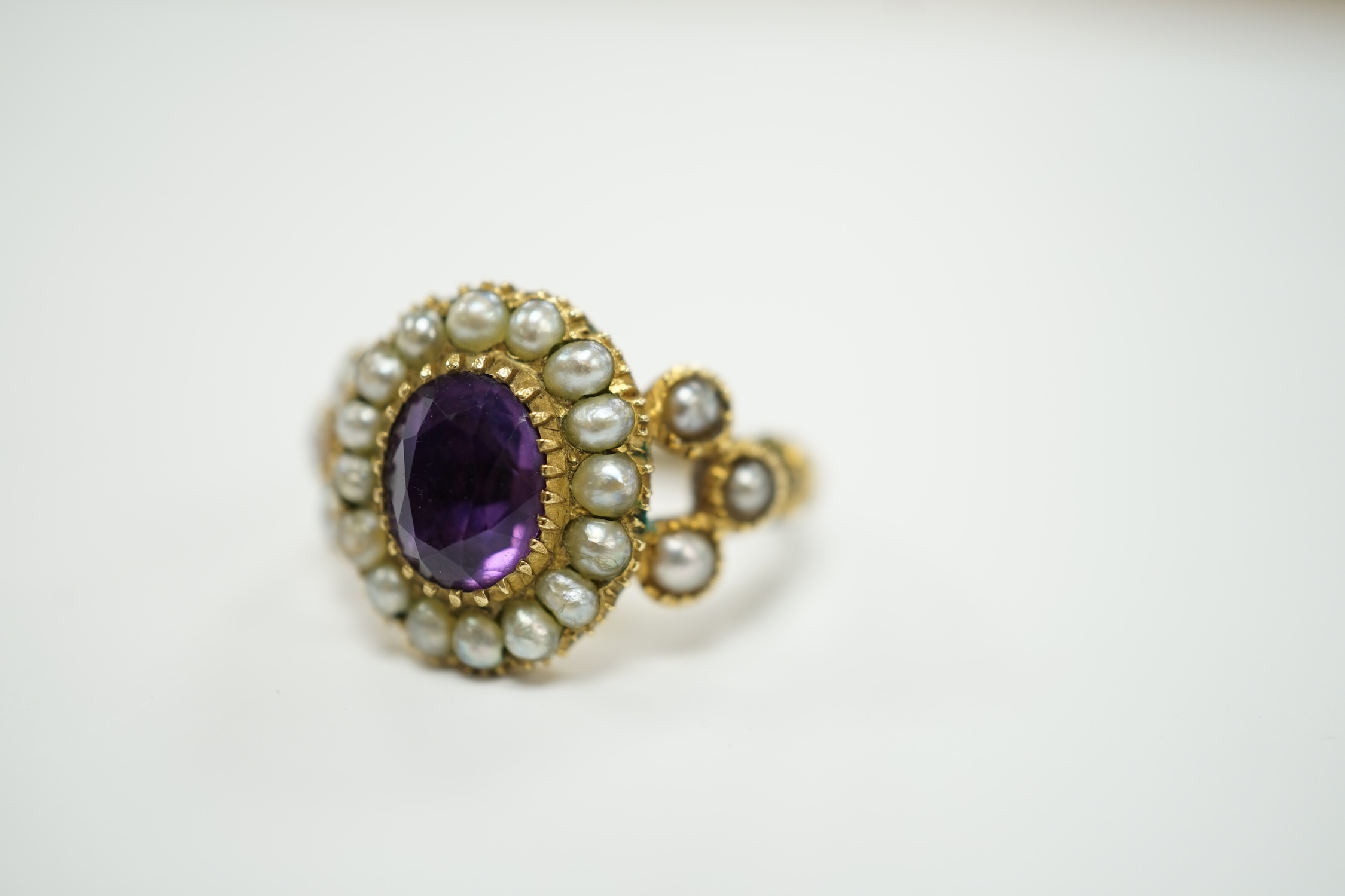 A Victorian yellow metal seed pearl and amethyst set oval cluster ring, size L, gross weight 3.7 grams.